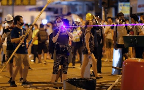 A woman uses a laser pointer beam on policemen as they face off at Sham Shui Po district - Credit: &nbsp;Vincent Thian/&nbsp;AP