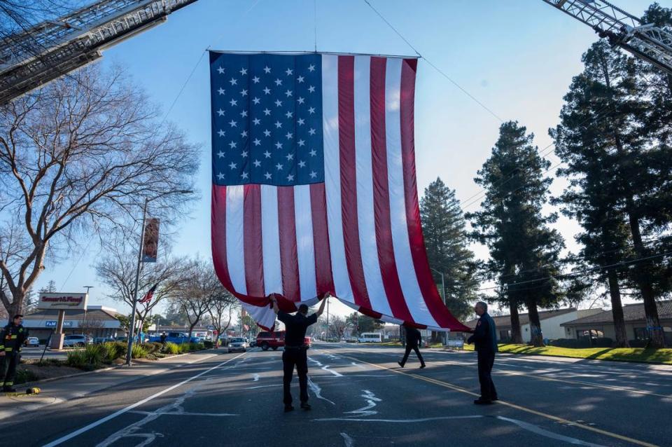 Members of the Cosumnes Fire Department help raise a flag on Elk Grove Boulevard as they prepare for a procession for fallen Elk Grove police officer Ty Lenehan on Tuesday, Jan. 25, 2022. Lenehan died after he collided with a wrong way driver on his way to work early Friday morning in Sacramento on Jan. 21.