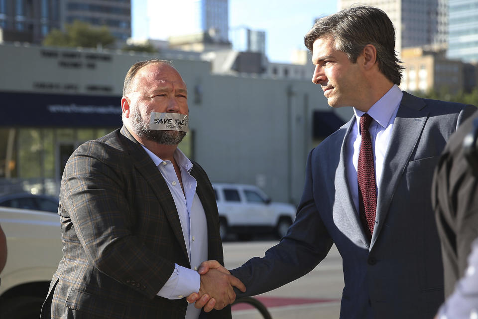 Alex Jones arrives at the Travis County Courthouse in Austin, Texas, Tuesday, July 26, 2022, with a piece of tape over his mouth that reads "save the 1st." He shook hands with his lawyer, Andino Reynal. An attorney for the parents of one of the children who were killed in the Sandy Hook Elementary School shooting told jurors that Jones repeatedly “lied and attacked the parents of murdered children” when he told his Infowars audience that the 2012 attack was a hoax. Attorney Mark Bankston said during his opening statement to determine damages against Jones that Jones created a “massive campaign of lies” and recruited “wild extremists from the fringes of the internet ... who were as cruel as Mr. Jones wanted them to be" to the victims' families. Jones later blasted the case, calling it a “show trial” and an assault on the First Amendment. (Briana Sanchez/Austin American-Statesman via AP, Pool)