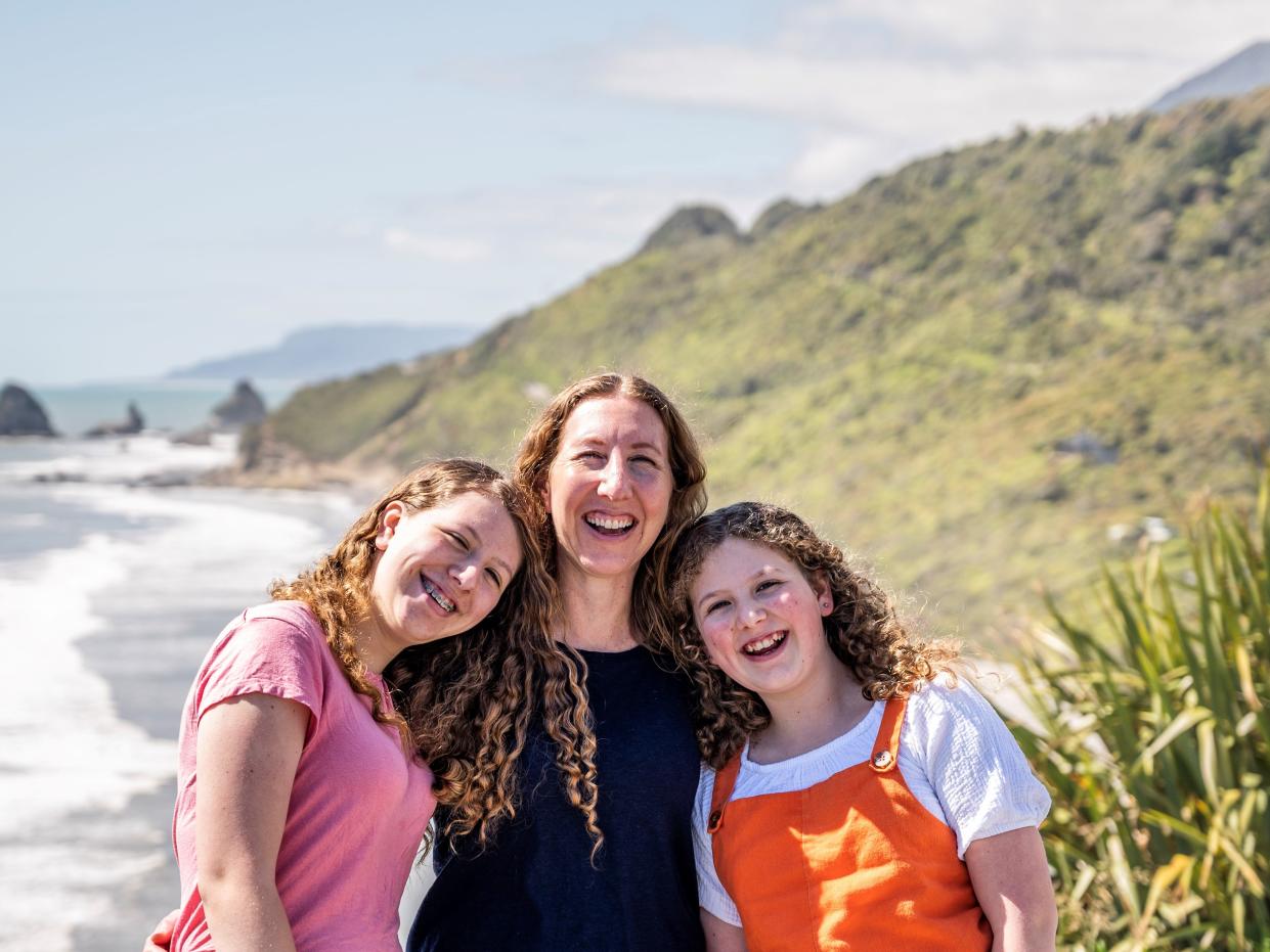 A woman and two girls pose in front of a coastal view.