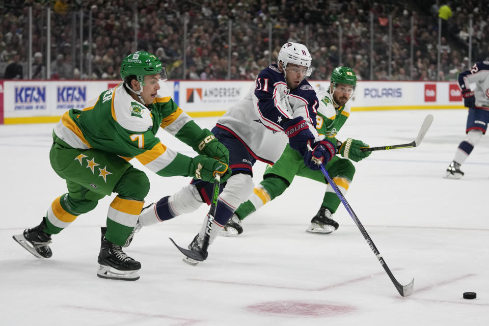 Columbus Blue Jackets center Adam Fantilli (11) battles for the puck against Minnesota Wild defenseman Brock Faber (7), left, and center Frederick Gaudreau (89), right, during the first period of an NHL hockey game Saturday, Oct. 21, 2023, in St. Paul, Minn. (AP Photo/Abbie Parr)