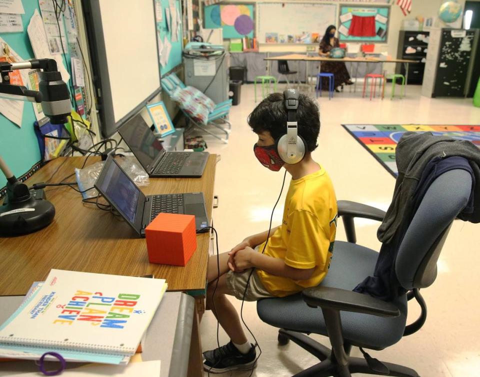 Nova Blanche Forman Elementary School teacher Attiya Batool teaches her fourth-grade class virtually as her son, Nabeel, does his second-grade classwork online wearing a mask and headphones during the first day of school in Broward, Wednesday, Aug. 19, 2020. All classes in Broward public schools are being taught remotely. The school district has made some adjustments where teachers may bring their child to their classroom to do remote learning while they teach their students under certain conditions.