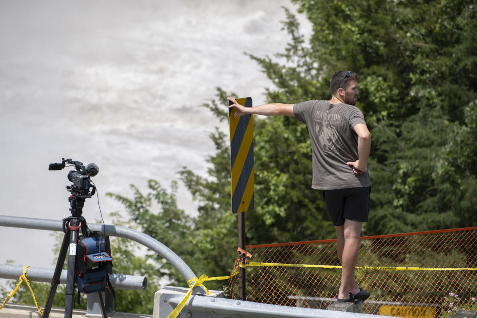 An onlooker stands on a road barrier as waters rush by the Rapidan Dam in Rapidan, Minn., Monday, June 24, 2024. Waters from the Blue Earth River diverted the dam amid recent heavy rainfalls. (Casey Ek/The Free Press via AP)