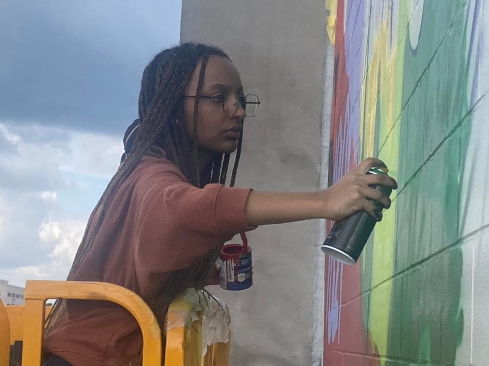 Helena Teferra, a sophomore at Springfield High School, uses spray paint on the "Local Heroes" mural at the new Springfield-Sangamon County Transportation Hub on the 10th Street corridor Sunday. Latex paint is being used as a primer with professional grade and UV resistant spray paint being applied on top of it. Teferra was among several students who helped with the installation over the weekend.