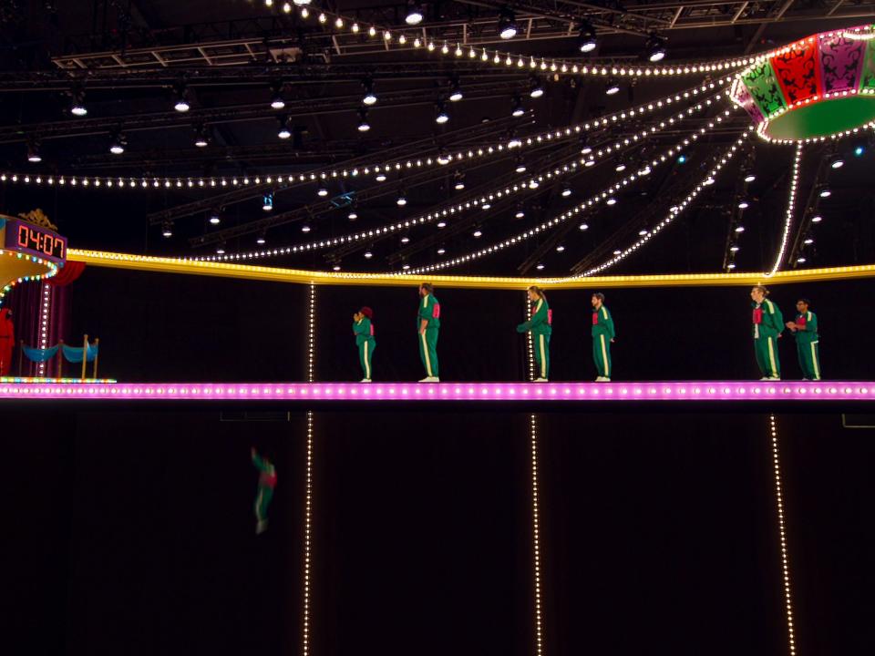 the glass bridge in squid game the challenge, a suspended brightly lit bridge in a circus tent like set