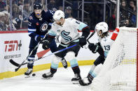 Seattle Kraken's Adam Larsson (6) and Brandon Tanev (13) battle for the puck against Winnipeg Jets' Mason Appleton (22) during the second period of an NHL hockey game in Winnipeg, Manitoba on Tuesday April 16, 2024. (Fred Greenslade/The Canadian Press via AP)