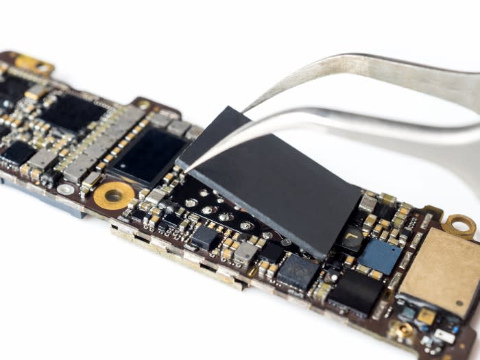 A smartphone logic board with a large chip being removed from it by a pair of pliers.