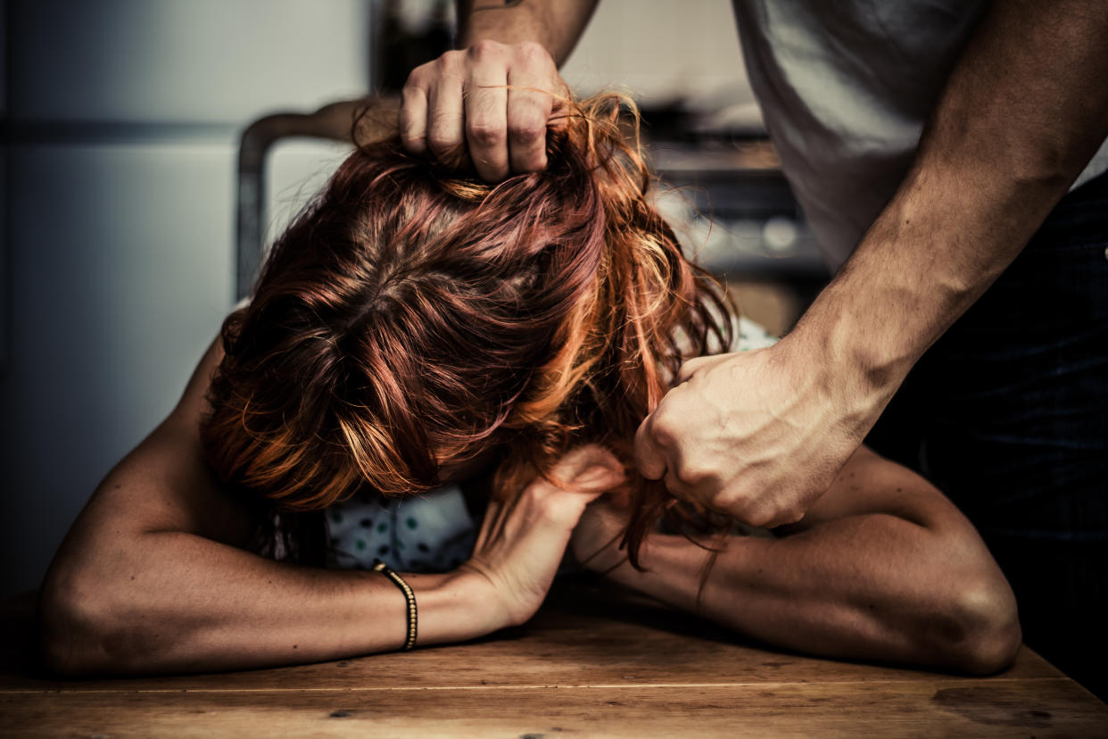 Young woman is crying at the kitchen table as her abusive boyfriend pulls her hair and threatens to hit her