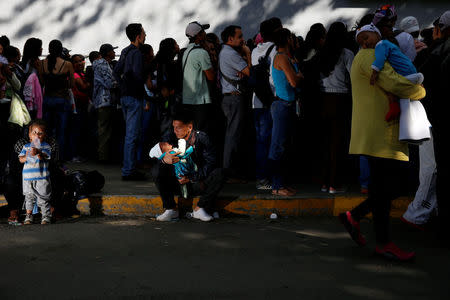 A man carrying a baby rests on the sidewalk as he queues to try and buy diapers outside a pharmacy in Caracas, Venezuela March 18, 2017. REUTERS/Carlos Garcia Rawlins