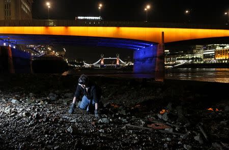 A mudlark uses a torch to look for objects under London Bridge on the bank of the River Thames in London, Britain June 06, 2016. REUTERS/Neil Hall