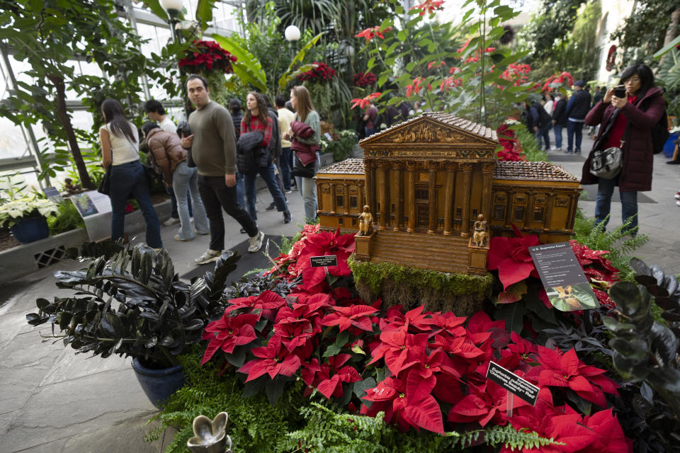 Visitors look at a replica of the U.S. Supreme Court adorned with different varieties of poinsettias on display at the Smithsonian's U.S. Botanical Garden, Saturday, Dec. 16, 2023, in Washington. (AP Photo/Manuel Balce Ceneta)