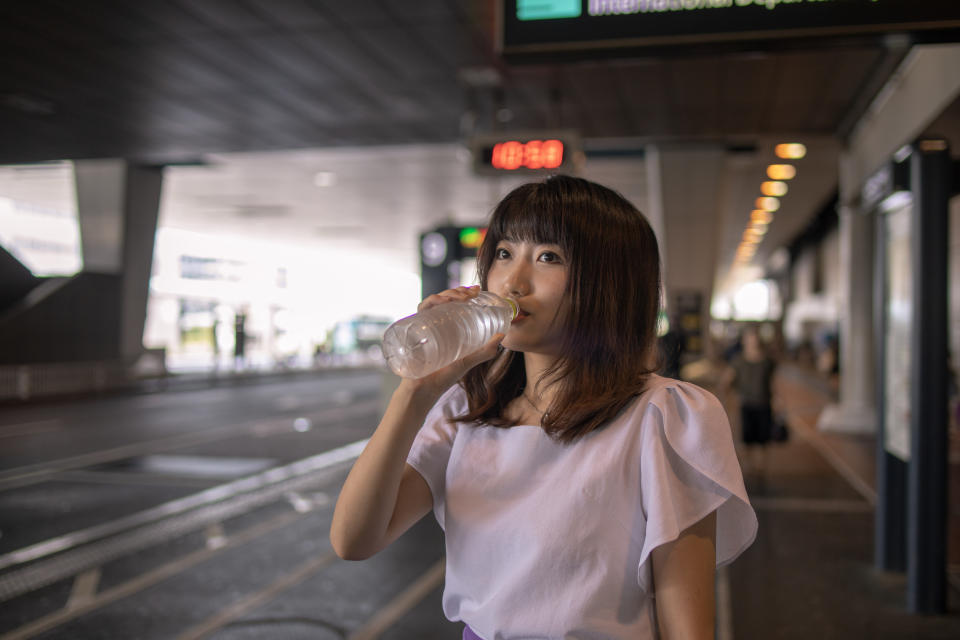 Young woman drinks a bottle of water at the airport bus station