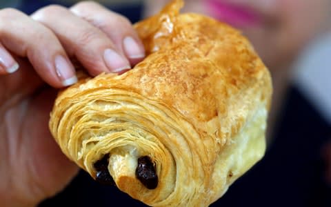 A baker holds a pain au chocolat, also called chocolatine in the Gascony region, in her bakery in Bordeaux, France, - Credit: REGIS DUVIGNAU/Reuters