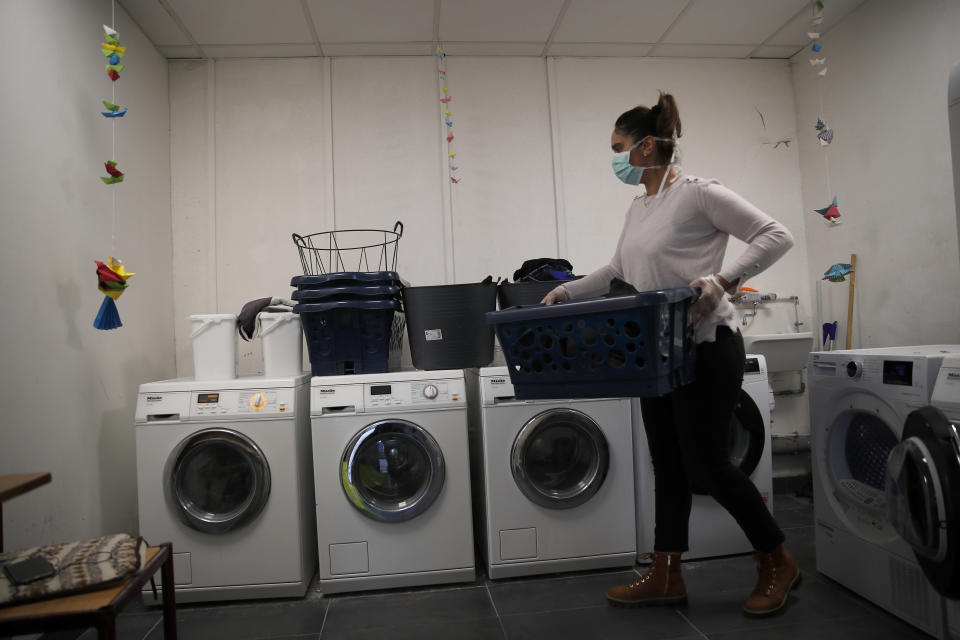 A volunteer helps to clean the clothes of homeless and migrants in the "Aurore" center in Paris, Thursday, April 2, 2020. Amid the coronavirus lockdown, charity workers at France's Aurore association, are preparing more than a thousand meals a day for migrants and the homeless on the half-abandoned grounds of a former Paris hospital whose patron saint was devoted to the poor. (AP Photo/Francois Mori)