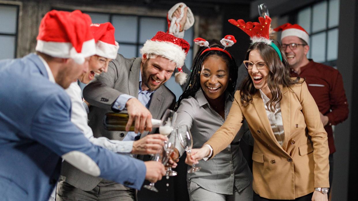  Smiling businessman pours champagne for his colleagues during a Christmas party in the office. 