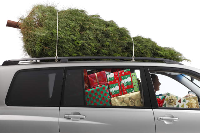 A woman driving a car filled with Christmas presents and a Christmas tree on top..To see more holiday images click on the link b