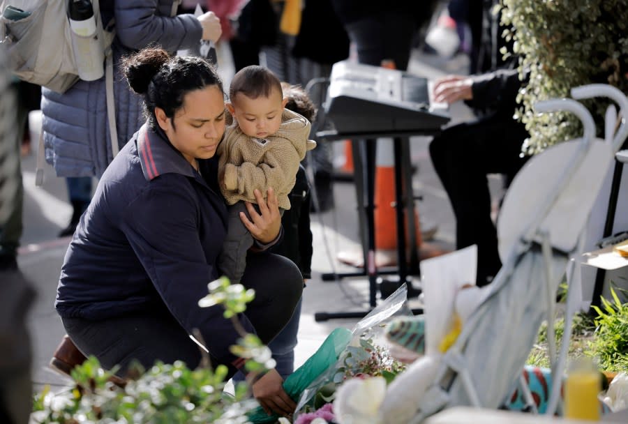 A woman places flowers in the growing memorial during a vigil, Monday, March 18, 2024, for those killed at a bus stop on West Portal Avenue in San Francisco. (Carlos Avila Gonzalez/San Francisco Chronicle via AP)