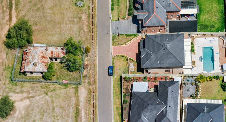 A road cuts between suburban houses and a country house.