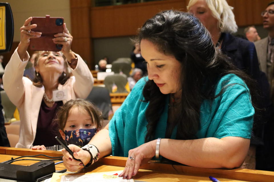  Rep. Linda Serrato (D-Santa Fe) signs into the official roster of state representatives as her daughter Alma watches on the first day of the 2023 Legislative Session. Serrato’s mother Rafaela Serrato is taking a picture with her phone. (Shaun Griswold/Source NM)