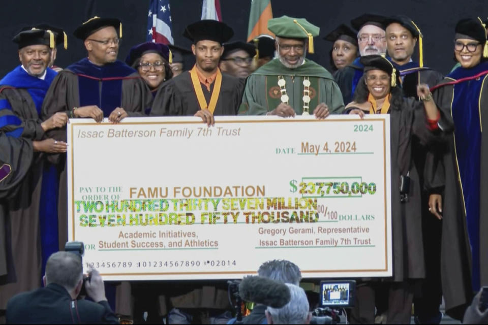 This image made from video provided by WCTV shows Gregory Gerami, a 30-year-old who called himself Texas' "youngest African American industrial hemp producer," fourth from left, and Florida A&M University president Larry Robinson pose with a ceremonial check while being surrounded by other university officials during a commencement ceremony on May 4, 2024 in Tallahassee, Fla. The $237 million donation was promised by Gerami, but everything was not what it seemed and the donation is now in limbo. Gerami maintains that everything will work out, but FAMU is not the only small university that has engaged with his major donation proposals only to see them go nowhere. (WCTV via AP)