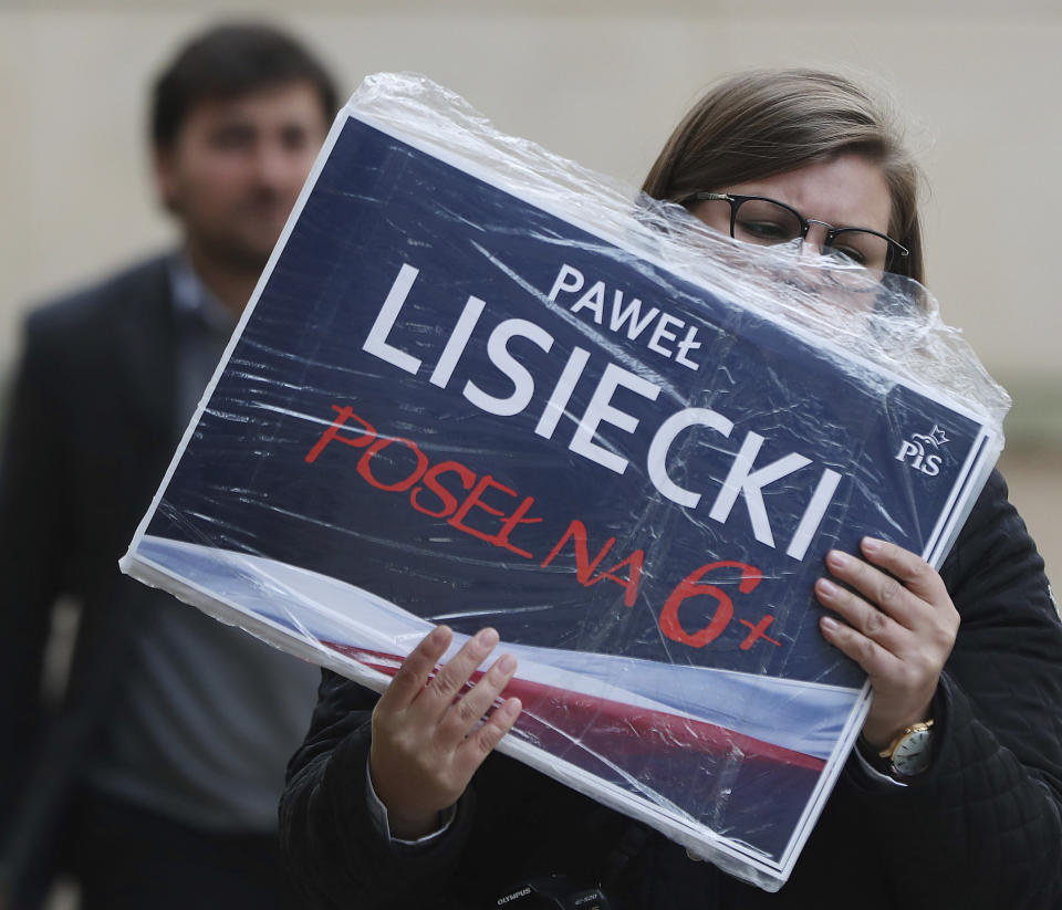 In this photo taken Tuesday Oct. 8, 2019 a supporter of Poland's ruling right-wing party is holding photos of one of the Law and Justice party's candidates at a convention in Warsaw, Poland, ahead of Sunday parliamentary election in which the party is hoping to win a second term in power.(AP Photo/Czarek Sokolowski)