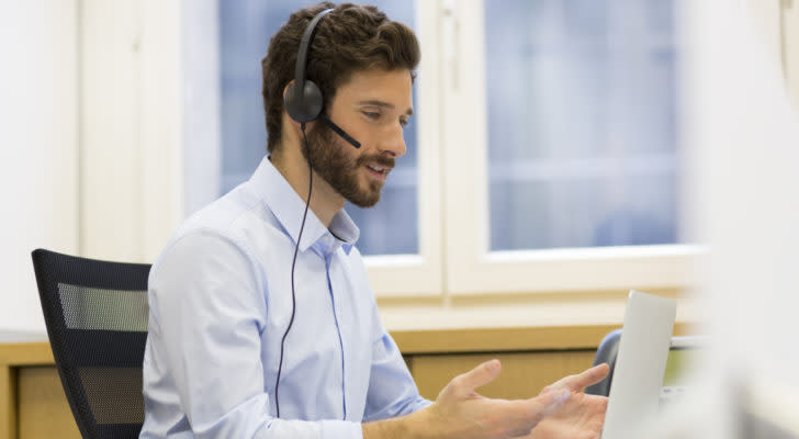 A man wearing a headset speaks to someone on a computer.