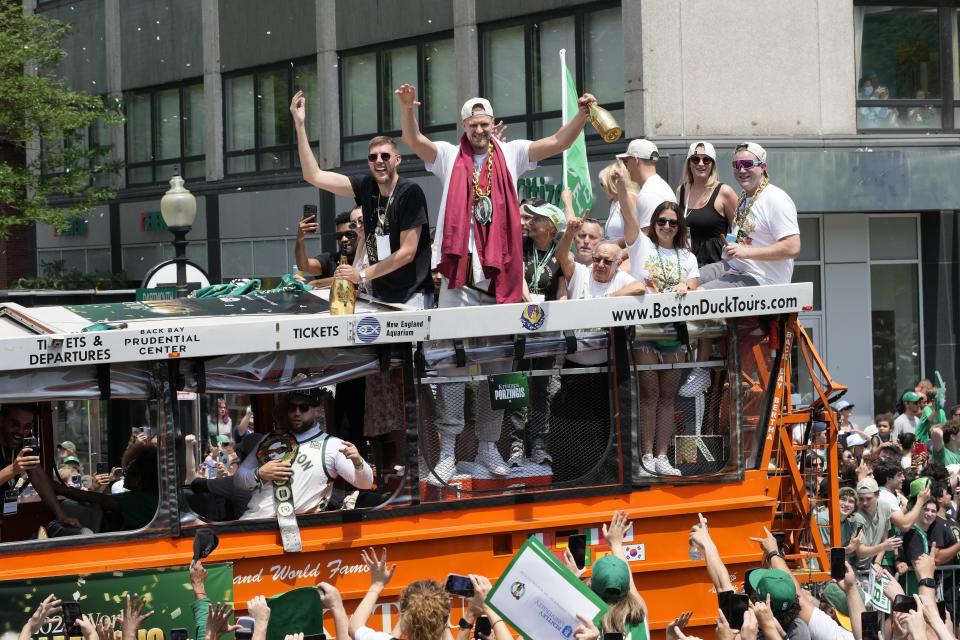 Boston Celtics' Kristaps Porzingis, center wearing the Celtics medallion, gestures to fans along the NBA championship team's duck boat parade Friday, June 21, 2024, in Boston. (AP Photo/Michael Dwyer)