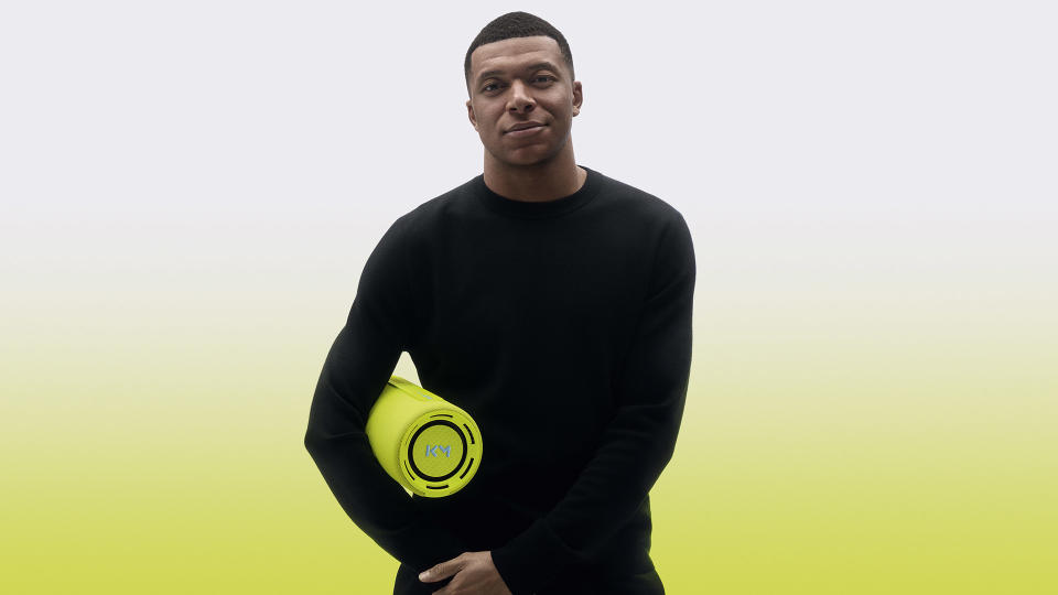 kylian mbappé stands holding a speaker udner his arm