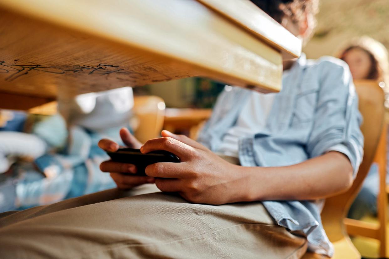 A student uses a cellphone under the table during a class at an elementary school.