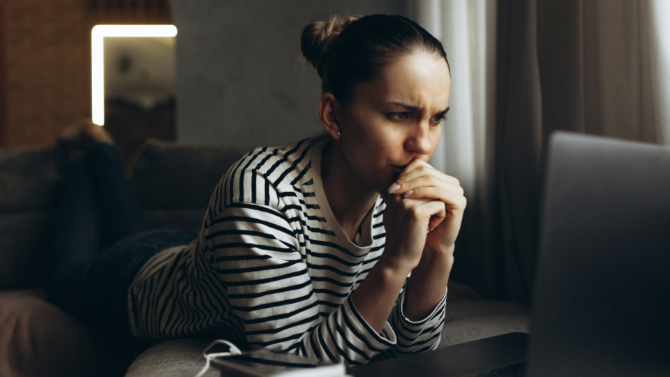 A woman staring at her laptop with a concerned expression to represent someone who has had their password stolen by cyber criminals.