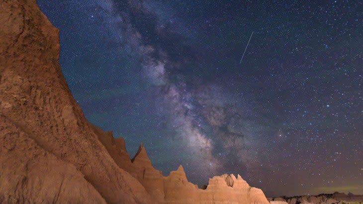 <span class="article__caption">Long exposure image of the Milky way shows a satellite streaking through the summer night sky over the Badlands, South Dakota. A passing car provides the lighting for the mountains in the foreground.</span> (: LiHotShots/iStock via Getty Images)