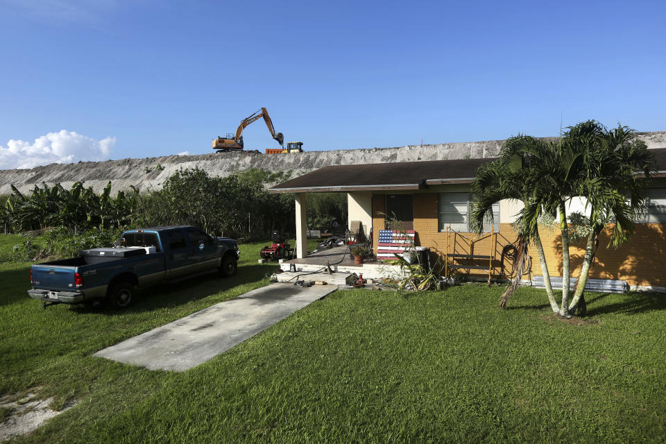 In this Friday, Nov. 1, 2019 photo, rehabilitation work takes place on top of the Herbert Hoover Dike surrounding Lake Okeechobee, just a few feet from a home in Pahokee, Fla. Hurricane tides overtopped the original dike in 1926 and 1928, washed away houses and caused over 2,500 deaths. (AP Photo/Robert F. Bukaty)