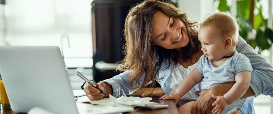 Young happy mother going through home finances and communicating with her baby son.