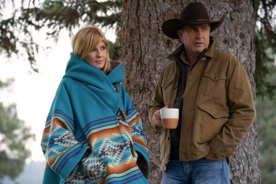 Kelly Reilly and Kevin Costner stand bundled near a tree