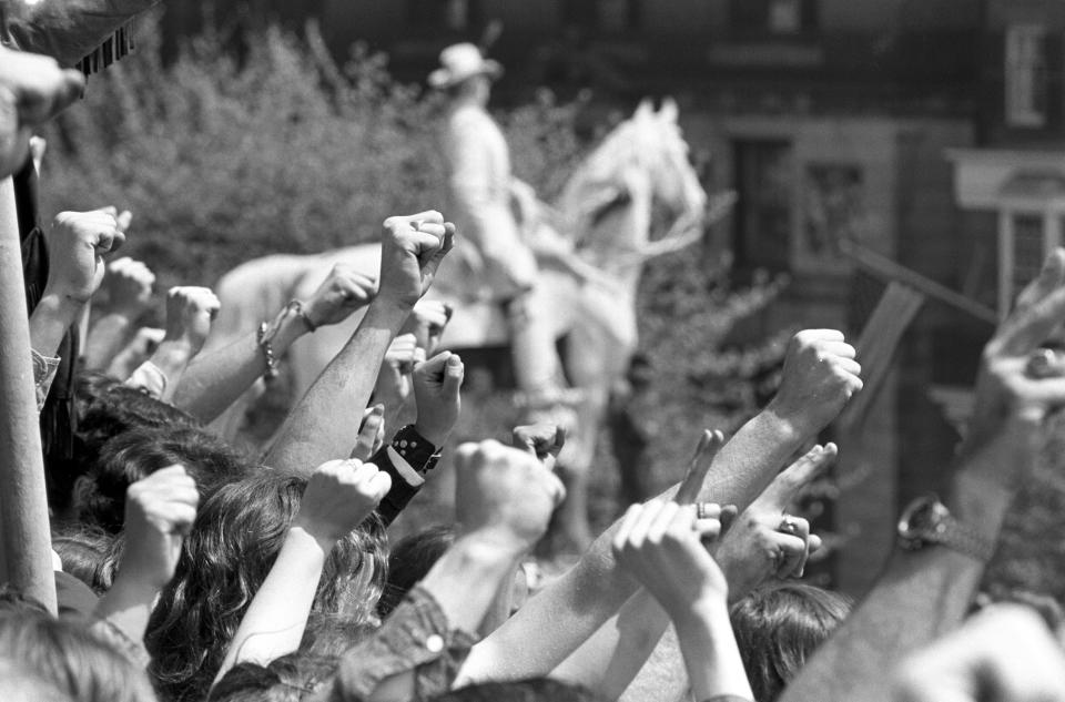 People raise their fists in the air during a protest with a statue in the Boston Common seen in the background