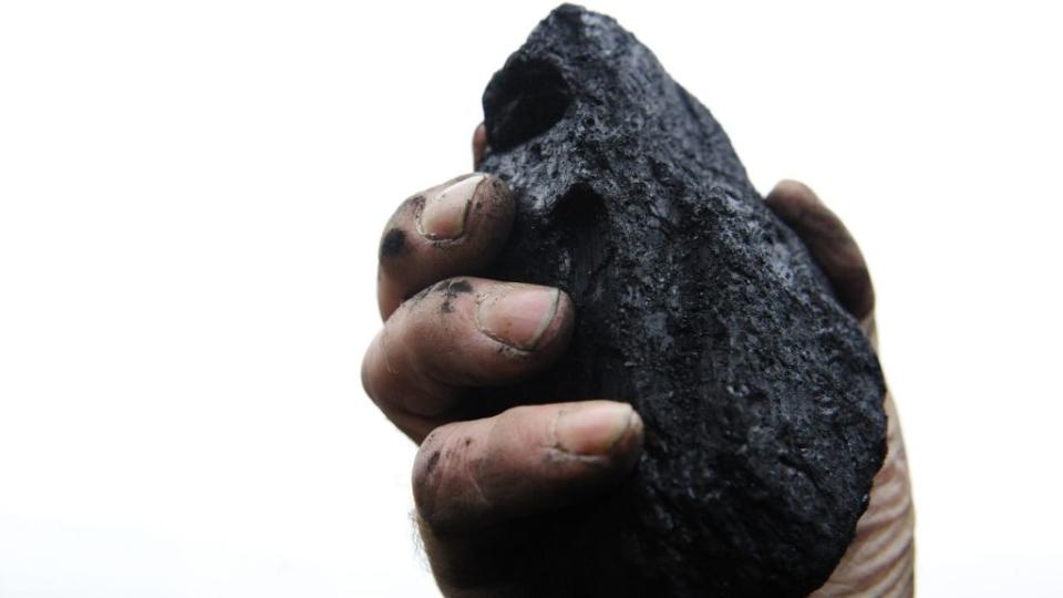 A coal merchant holds up a lump of coal.