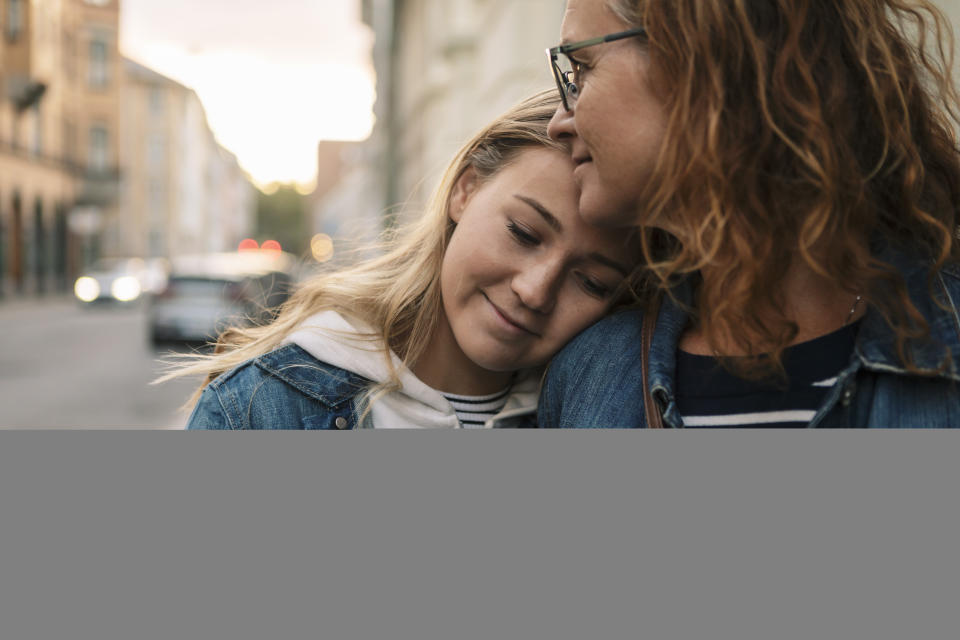 A teenage girl resting her head on her mother's shoulder