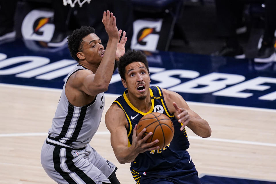 Indiana Pacers guard Malcolm Brogdon, right, shoots in front of San Antonio Spurs forward Keldon Johnson, right, during the first half of an NBA basketball game in Indianapolis, Monday, April 19, 2021. (AP Photo/Michael Conroy)