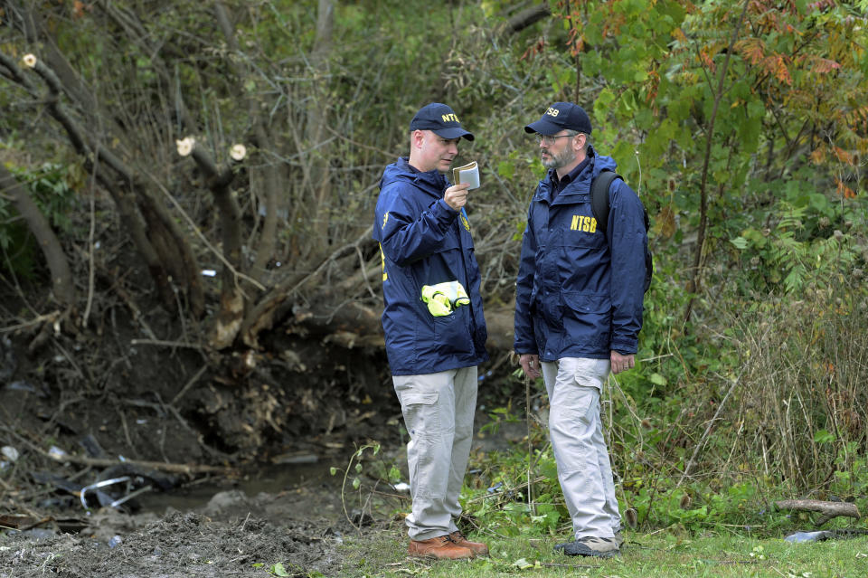 FILE - In this Oct. 7, 2018 file photo, members of the National Transportation Safety Board work at the scene of a fatal limousine crash in Schoharie, N.Y. A memorial to the 20 people killed when a stretch limousine blew through an intersection at the bottom of a long hill and barreled into an earthen embankment a year ago is being unveiled at the crash site in upstate New York. The memorial featuring 20 stones in a semicircle is to be viewed privately by family members and first responders Saturday morning, Oct. 5, 2019. (AP Photo/Hans Pennink, File)