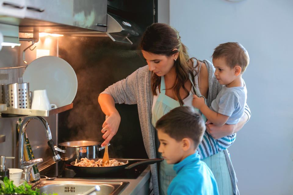 A woman cooks while watching her two young sons