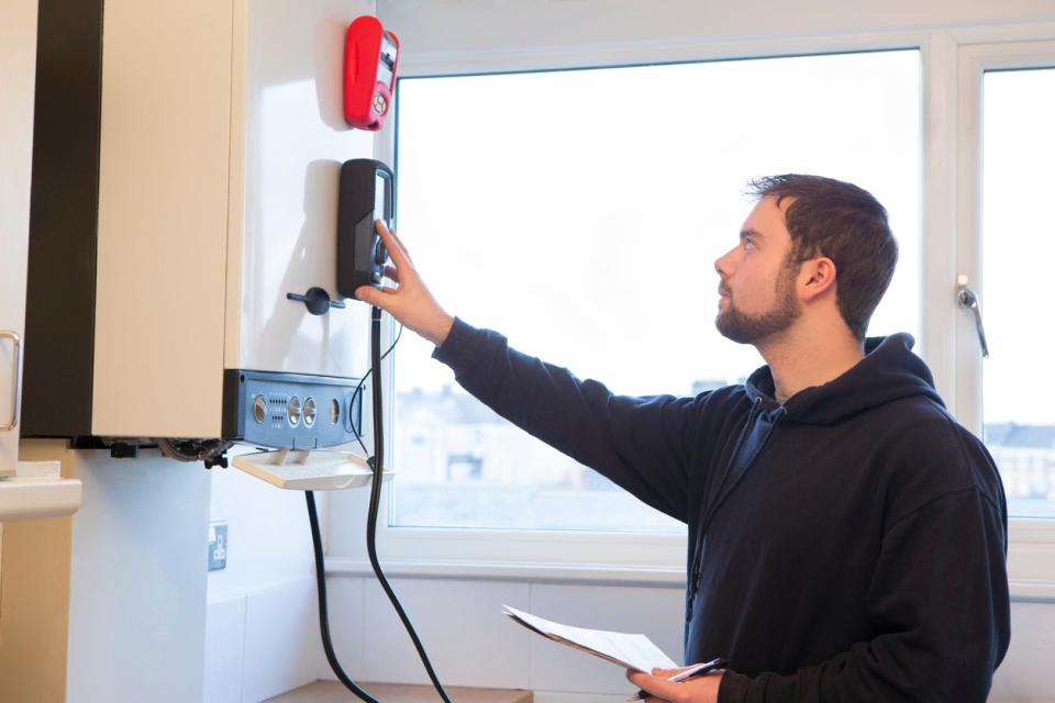 A man is standing checking the gas central heating boiler in a home.