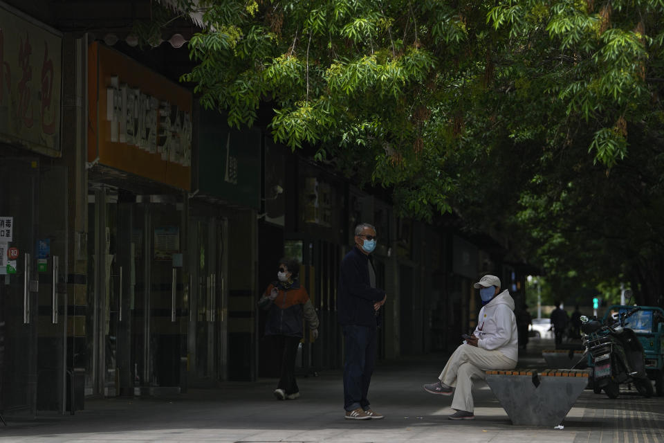 Residents wearing face masks take a rest near shuttered retail shops after authorities ordered the closure of non-essential businesses and asked people to work at home in the Chaoyang district on Monday, May 9, 2022, in Beijing. (AP Photo/Andy Wong)