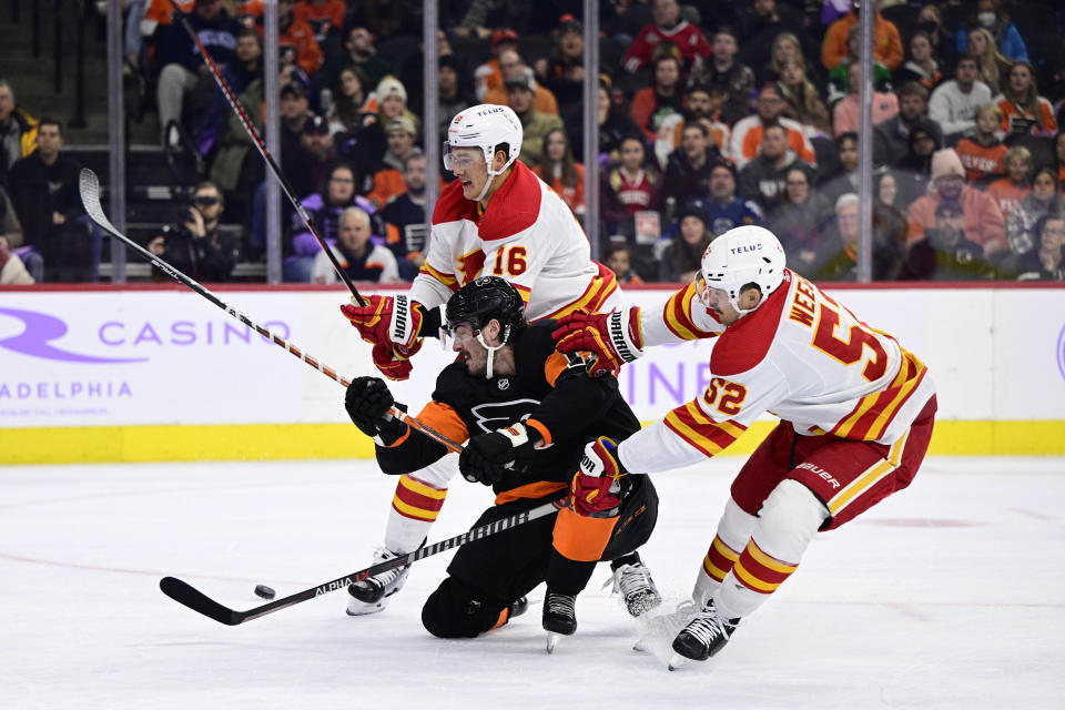 Calgary Flames' Nikita Zadorov rear, and MacKenzie Weegar (52) knock the puck from Philadelphia Flyers' Zack MacEwen, center, during the second period of an NHL hockey game, Monday, Nov. 21, 2022, in Philadelphia. (AP Photo/Derik Hamilton)