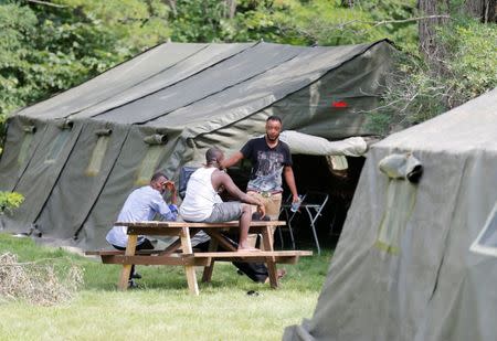 Refugees sit outside one of the tents set up to house the influx of asylum seekers by the Canadian Armed Forces near the border in Lacolle, Quebec, Canada August 10, 2017. REUTERS/Christinne Muschi