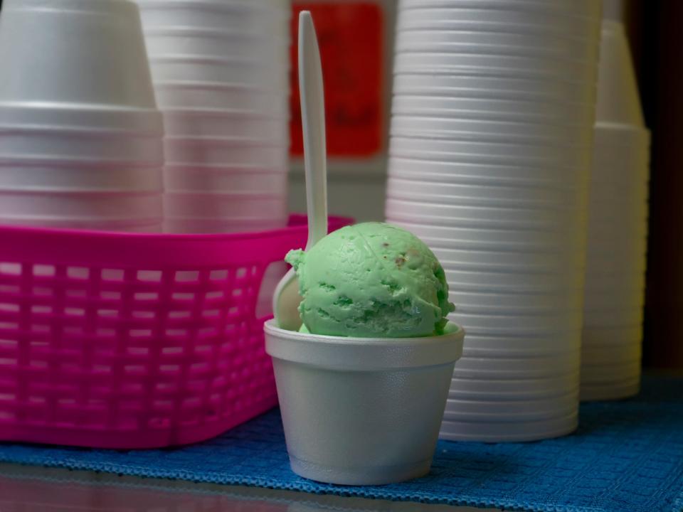 pistachio ice cream in a styrofoam container next to a stack of styrofoam cups