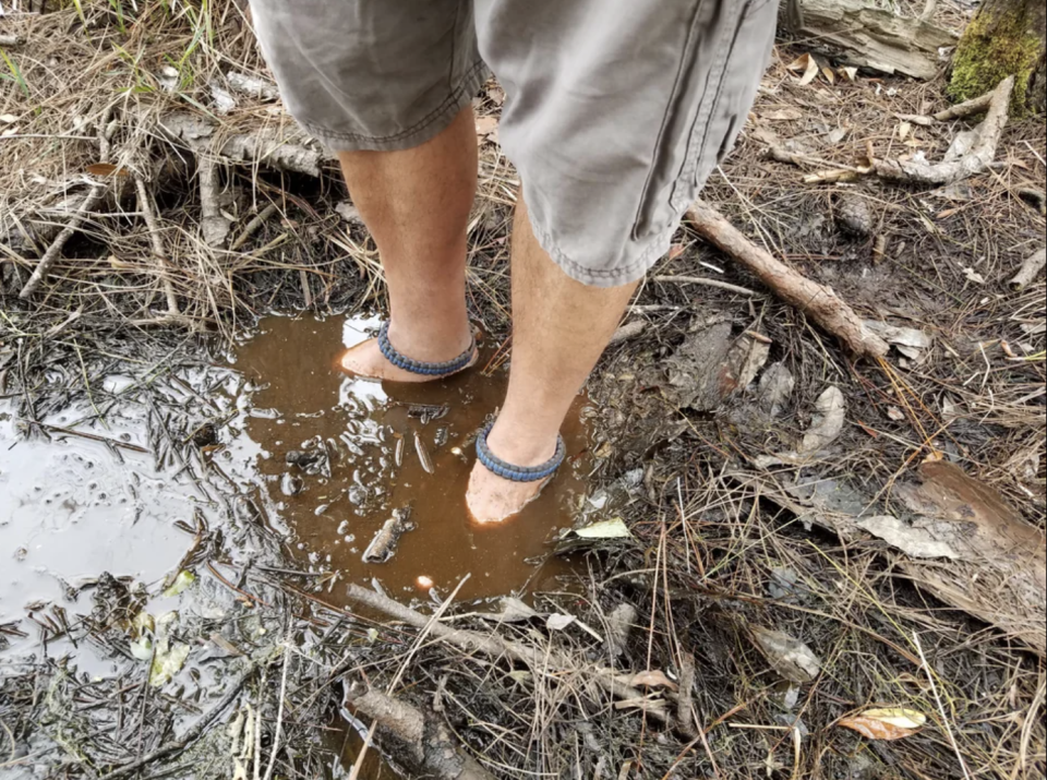 A man has his bare feet submerged in a muddy puddle