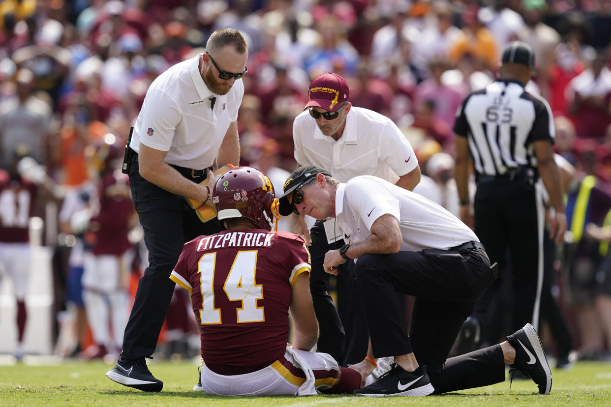 Members of the Washington Football Team staff check on condition of quarterback Ryan Fitzpatrick (14) after he was injured on a hit by Los Angeles Chargers linebacker Uchenna Nwosu during the first half of an NFL football game, Sunday, Sept. 12, 2021, in Landover, Md. (AP Photo/Alex Brandon)