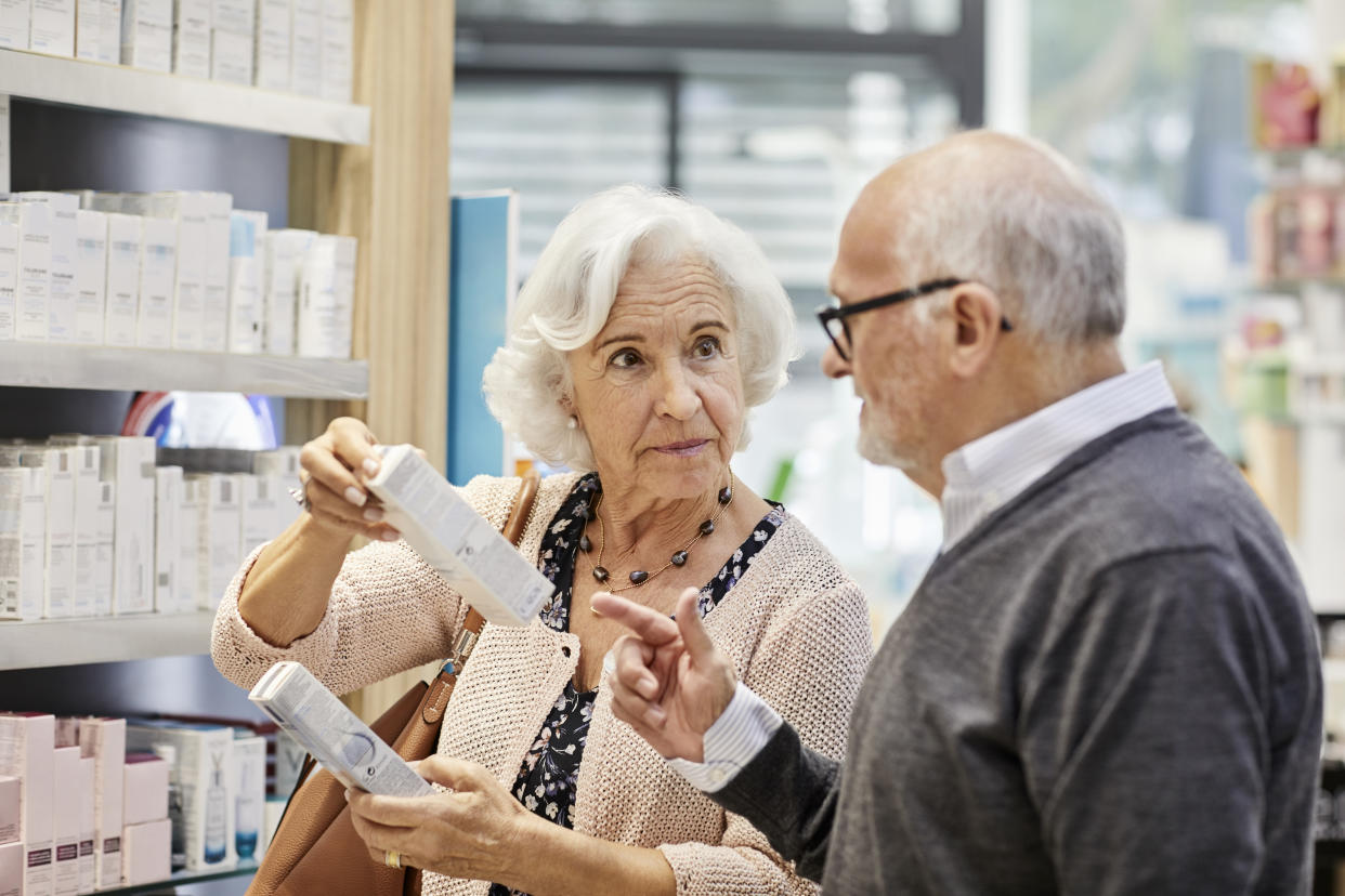 Elderly woman discussing over medicine with man at store. Senior couple is buying merchandise. They are wearing sweaters in pharmacy.