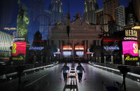 FILE - In this April 18, 2020, file photo, a lone worker wearing a mask cleans a pedestrian walkway devoid of the usual crowds as casinos and other business are shuttered due to the coronavirus outbreak in Las Vegas. Cards will be cut, dice will roll and jackpots jingle when casinos in Las Vegas and Nevada begin reopening at 12:01 a.m. on Thursday, June 4, 2020. There will be big splashes, even amid ongoing unrest, and big hopes for recovery from an unprecedented and expensive closure prompted by the coronavirus pandemic. (AP Photo/John Locher, File)