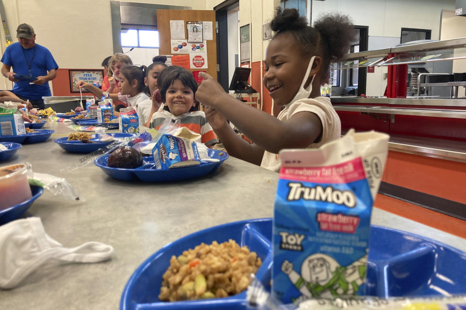 Half a dozen young students eat lunch at a school cafeteria table.
